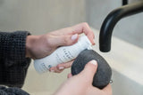 A woman applying a soothing milk cleanser for sensitive skin to a Bamboo Charcoal Konjac Sponge.