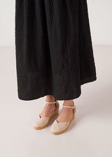 Beige canvas ankle-strap wedge espadrilles with a natural jute platform, styled with a black midi dress