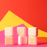 Stack of pink shower steamers against a vibrant red and yellow geometric background