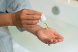A close-up image of a woman dispensing a gold-coloured serum for dry skin into her hand.