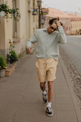 Man Walking Up A Street Wearing Mustard Linen Shorts And Sage Green Shirt