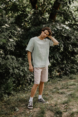 Man Facing Forward In Nature Wearing A Sage Green Linen Top And Light Linen Shorts