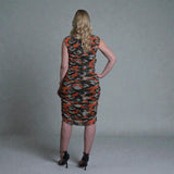 Woman wearing a sleeveless orange camouflage dress against a plain background
