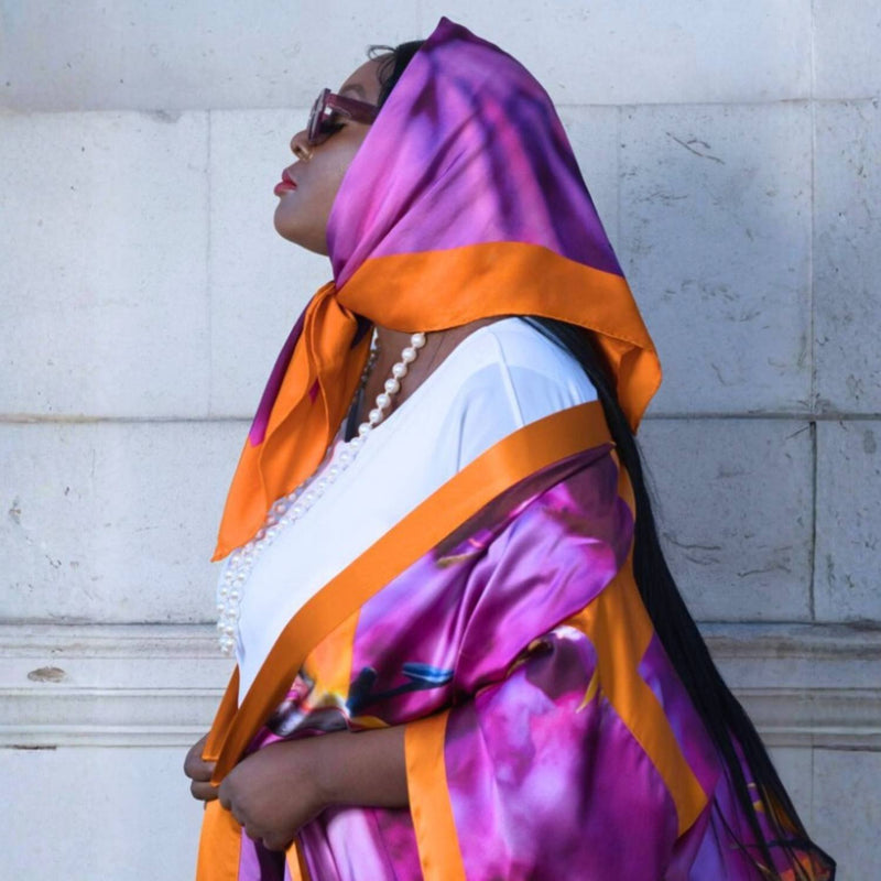 Woman wearing a colorful Bird of Paradise Pink Purple Silk Scarf  and white top against a light gray wall