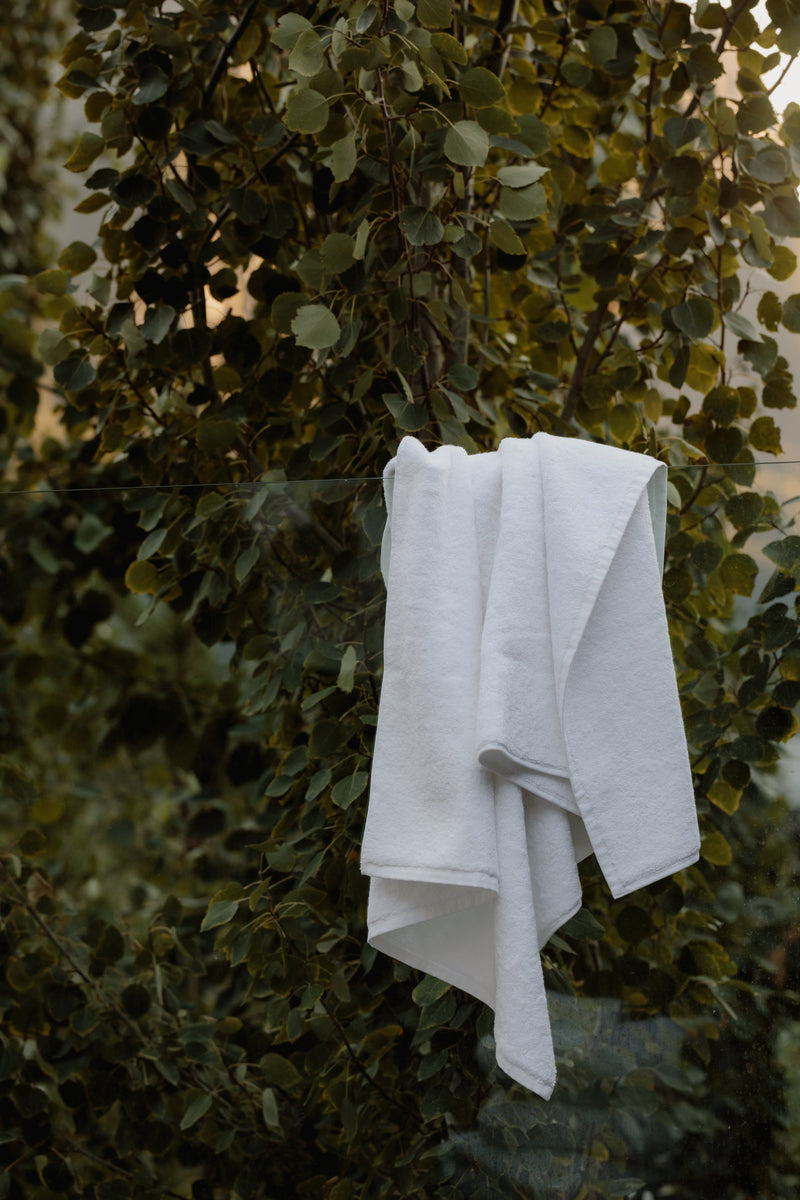 White bath towel handing on an outdoor glass wall - Organic towel by Takasa
