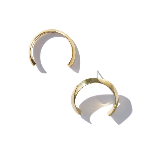 An untraditional hoop earring with a bold silhouette and eye-catching knife edge, handcrafted from upcycled brass.